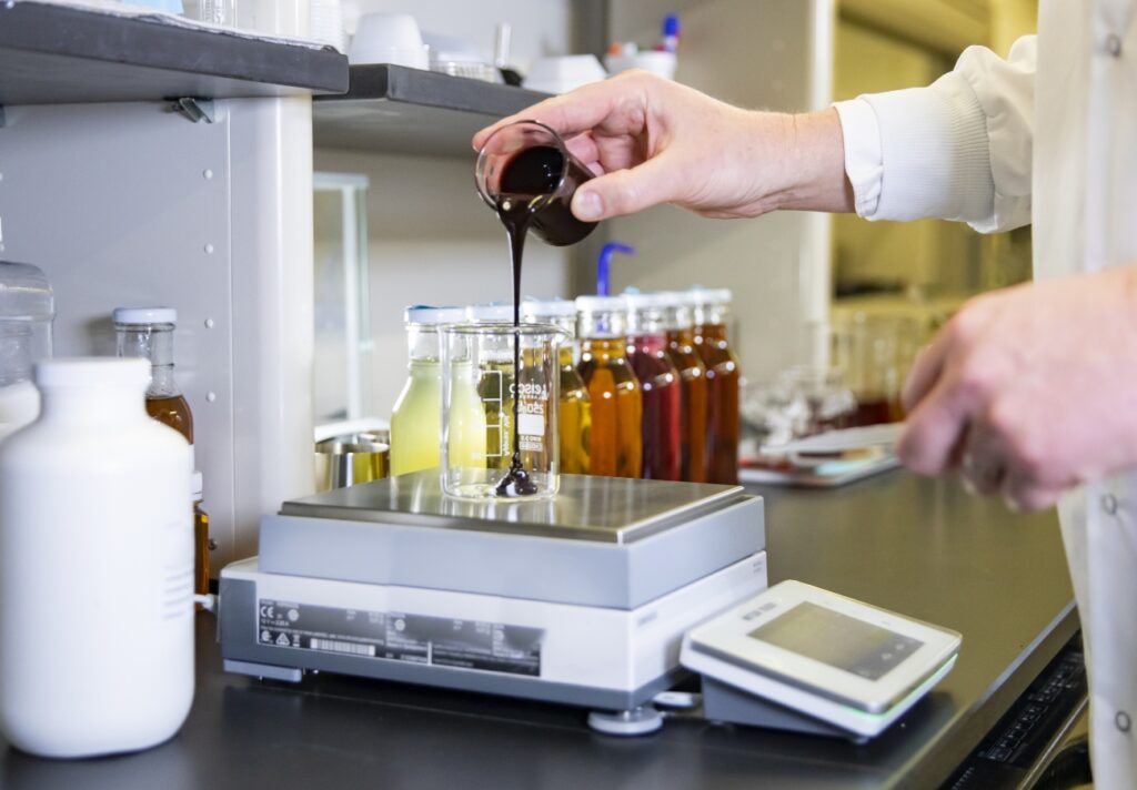 person pouring liquid ingredients into a beaker in a laboratory