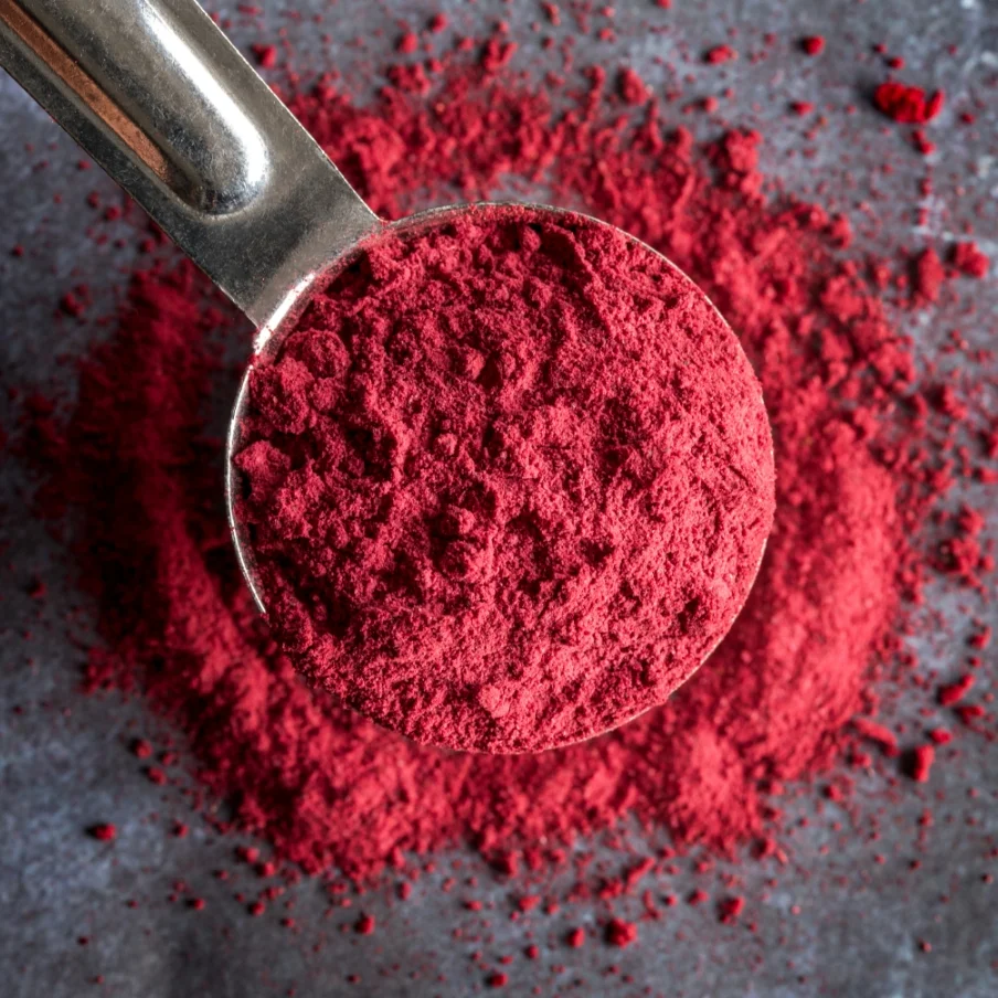 spoon filled with red powder on top of a table, which may be used as an ingredient in beverages or for manufacturing purposes
