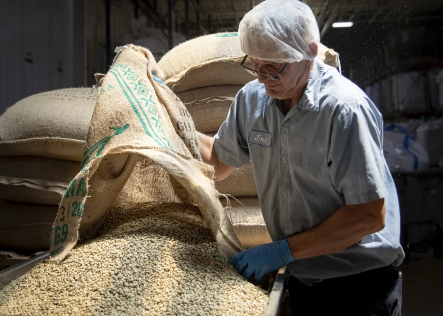 man standing in front of a bag of grain used as ingredients in manufacturing beverages