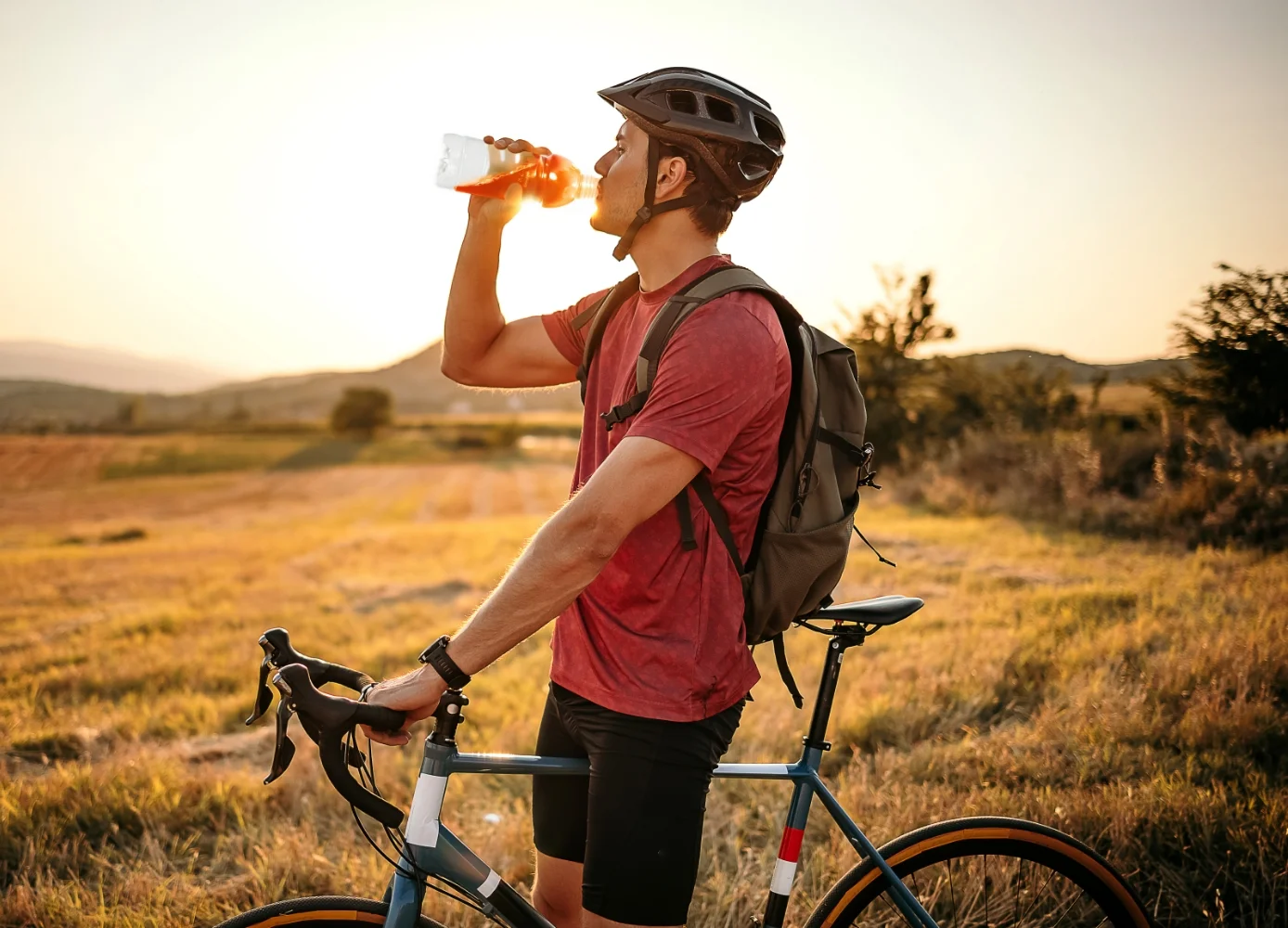 man in a red shirt is drinking a beverage from a bottle