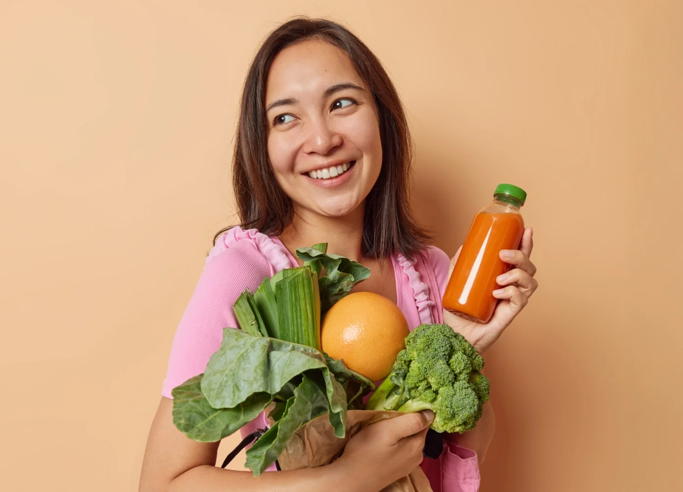woman holding a bottle of juice and fresh ingredients like vegetables