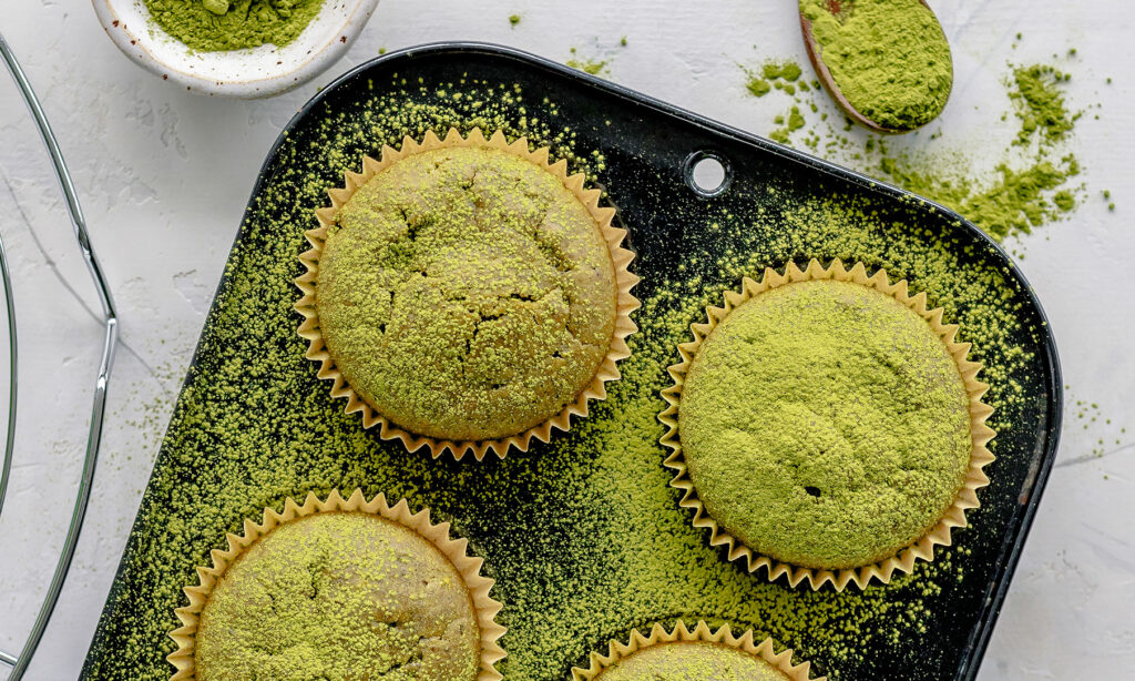 Matcha muffins dusted with green tea powder in a baking tray.