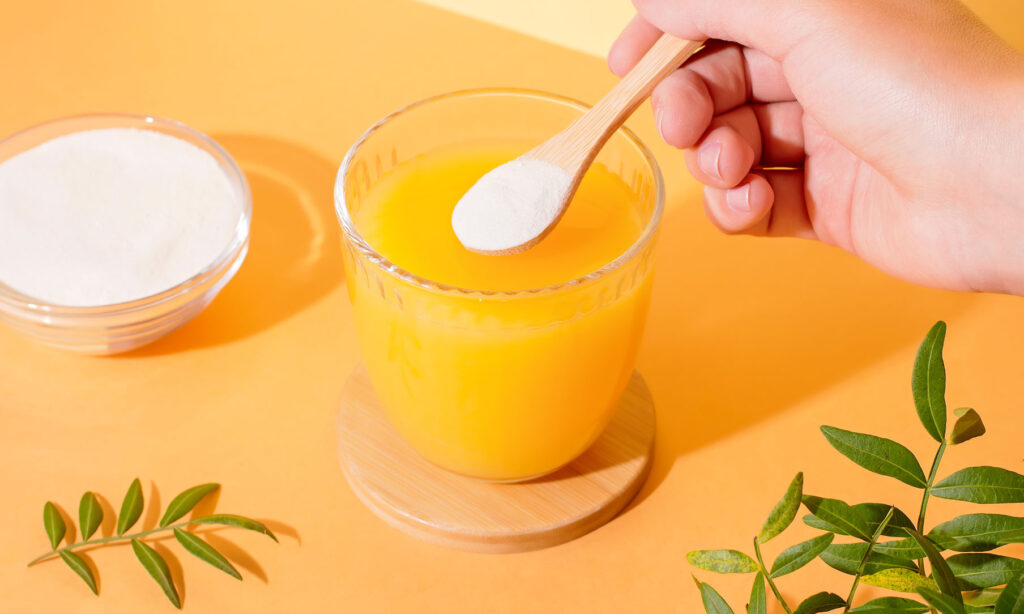 Person adding acerola cherry vitamin C powder to a glass of orange juice.
