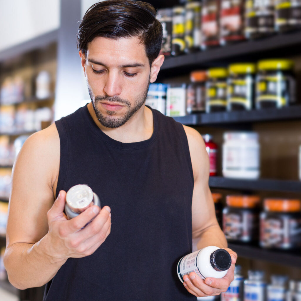 Shopper comparing supplement bottle labels in a store aisle.